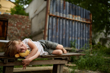 Unfortunate stray kid lying on the board in the dirty alley, shallow depth of field.