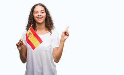 Young hispanic woman holding flag of Spain very happy pointing with hand and finger to the side