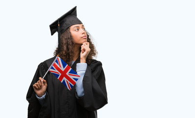 Young hispanic woman wearing graduation uniform holding flag of UK serious face thinking about question, very confused idea
