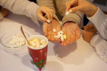 Obraz na płótnie Canvas Children's hands hold pieces of marshmallows and throw them in cocoa