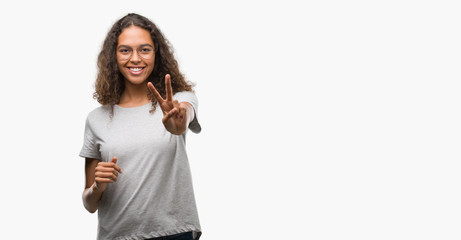 Beautiful young hispanic woman wearing glasses smiling looking to the camera showing fingers doing...