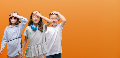 Group of boy and girls kids over orange background stressed with hand on head, shocked with shame...
