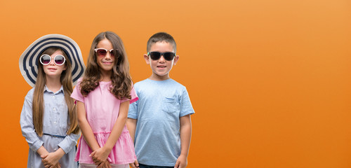 Group of boy and girls kids over orange background with a happy face standing and smiling with a...