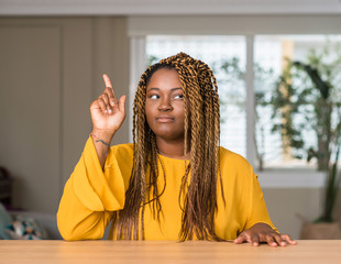 African american woman at home surprised with an idea or question pointing finger with happy face,...
