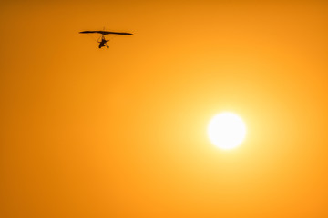 Motor glider flying high in orange sunset sky on sun disc background