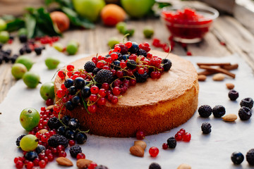 Process of preparation of biscuit with forest berries. Sponge cake. Biscuit strewn with berries and rubbed with powdered sugar on a wooden table. Country food.
