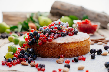 Process of preparation of biscuit with forest berries. Sponge cake. Biscuit strewn with berries and rubbed with powdered sugar on a wooden table. Country food.