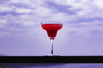 A glass with a red drink stands on the railing of the terrace against the background of the evening sky.
