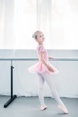 adorable little ballerina in pink tutu practicing ballet and looking away