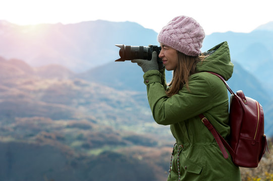 Charming young positive woman in autumn clothes with camera in hands while traveling through beautiful natural places. Concept of travel