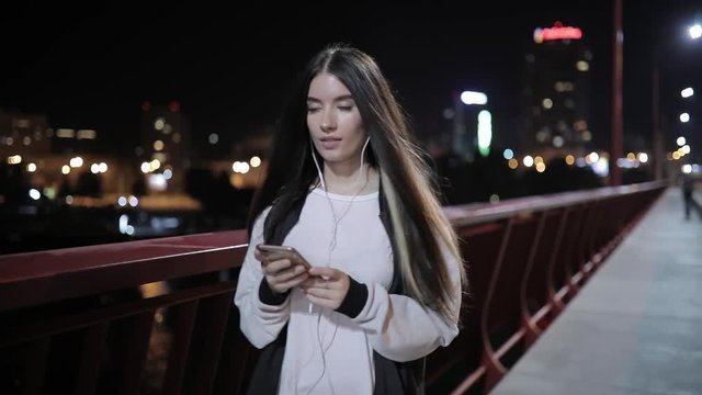 Woman listening to music walking on a bridge at midnight