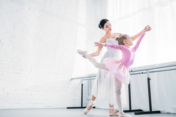 low angle view of adult ballerina training with child in pink tutu in ballet studio