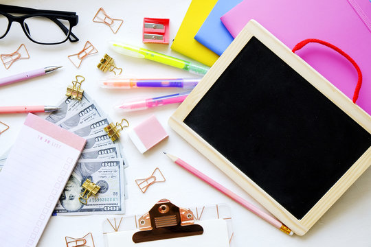 Educations costs. Stack of multiple one hundred dollar bills, planner notebook empty check box, colorful pens, school supplies, blank screen tablet, glasses. Background, flat lay, close up, copy space