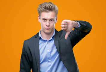 Young handsome blond business man with angry face, negative sign showing dislike with thumbs down,...