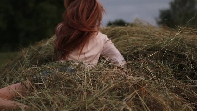 Young woman runs across meadow, jumps to haystack and she has fun and relax.