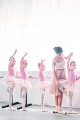 young woman teaching adorable kids dancing in ballet school