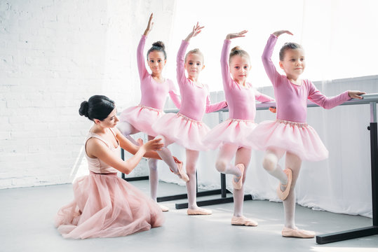 young woman teaching adorable children dancing in ballet school
