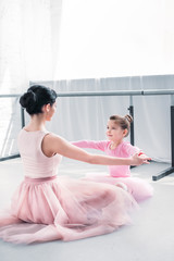 Naklejka premium young ballet teacher and little student in pink tutu skirts training together in ballet school