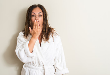 Beautiful middle age woman, wet hair wearing a towel cover mouth with hand shocked with shame for...
