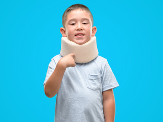 Dark haired little child injured wearing neck collar very happy pointing with hand and finger