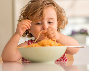 Beautiful blond child eating spaghetti with hands at home