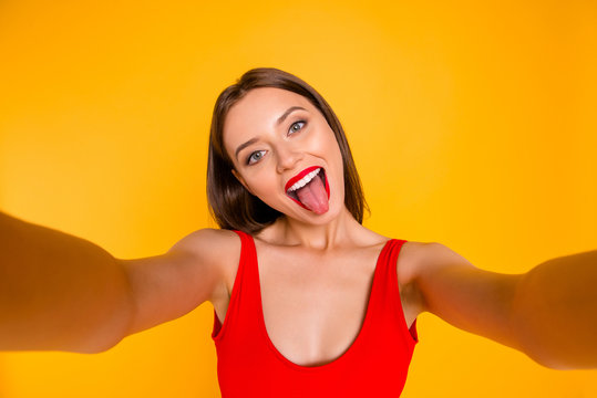 Close up portrait of emotional girl taking selfie shot, grimacing makes memories at holiday and for her blog isolated on bright yellow background