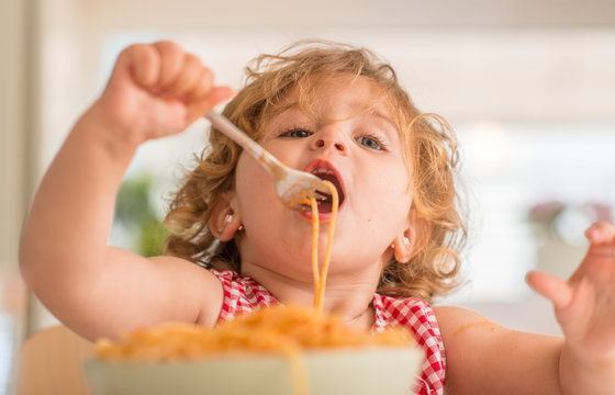 Beautiful blond child eating spaghetti with fork at home