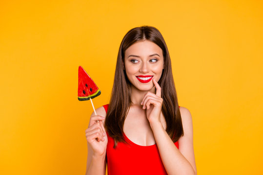 To be or not to be? Close up portrait happy and cute young woman holding piece on caramel fruit on stick, looking thoughtfully aside isolated on bright yellow background