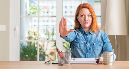 Redhead woman studying at home with open hand doing stop sign with serious and confident...