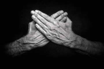 Black and White photo of crossed man's hands on dark background, symbolizing protection of security