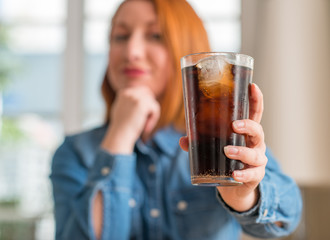 Redhead woman holding soda refreshment serious face thinking about question, very confused idea