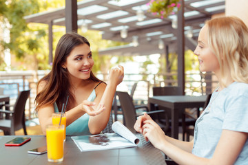 Two beautiful young girls sitting by the table in cafe