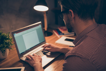 Back angle, close up portrait of attractive, hard worker, busy man in shirt with hairstyle, stubble working at night, taking work at home, sitting in work place, station holding hands on keypad