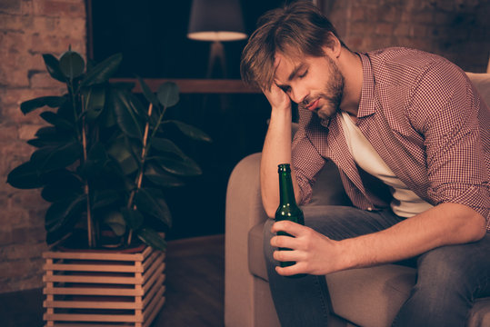 Portrait of unlucky, upset, tired, attractive, frustrated man holding bottle of beer in hand touching his head with arm having close eyes, bad luck, alcohol addiction, relationship problems
