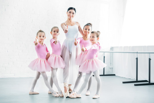 little ballerinas and ballet teacher showing thumbs up and smiling at camera in ballet school