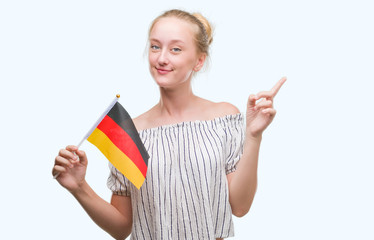 Blonde teenager woman holding flag of Germany very happy pointing with hand and finger to the side