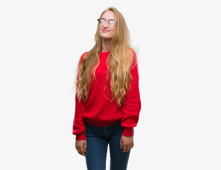 Blonde teenager woman wearing red sweater winking looking at the camera with sexy expression, cheerful and happy face.