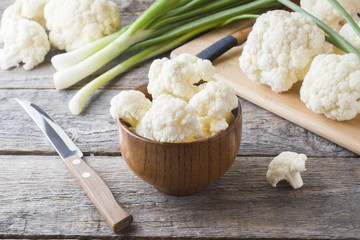 Fresh organic cauliflower, cut into pieces with green onion and knife on wooden background