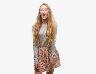 Blonde teenager woman wearing flowers skirt afraid and shocked with surprise expression, fear and excited face.