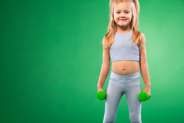 Kid girl doing fitness or yoga exercises with dumbbells isolated on green background