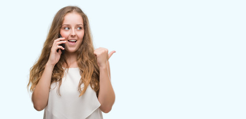 Young blonde woman using smartphone pointing and showing with thumb up to the side with happy face...