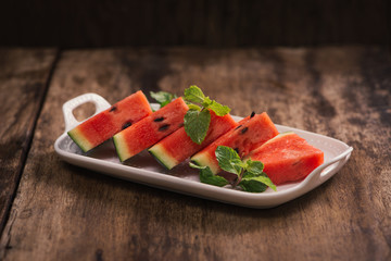 Fresh sliced watermelon in white dish on wooden table.
