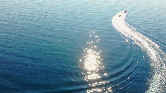Aerial view of high speed boat pulls the banana boat on blue sea. Drone shot flying over people who enjoy in water sports