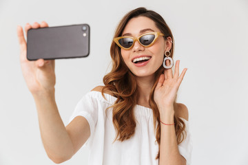 Photo of pretty european woman 20s wearing sunglasses taking selfie on smartphone, and touching...
