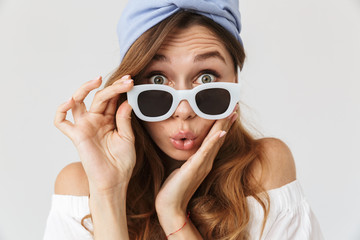 Photo closeup of surprised stylish woman 20s looking at camera from under sunglasses, isolated over white background