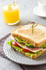 Sandwich with cheese, ham and fresh vegetables on a plate. Fresh juice and a Cup of coffee. The concept of Breakfast.