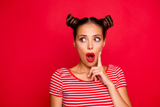 OMG! Close up face of shocked astonished girl with modern hairdo having wide open mouth and brown eyes looking at camera and to touch her cheek by finger isolated on red background with copyspace