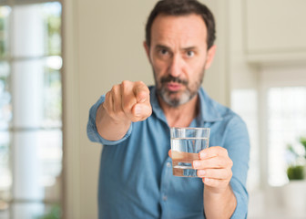Middle age man drinking a glass of water pointing with finger to the camera and to you, hand sign, positive and confident gesture from the front