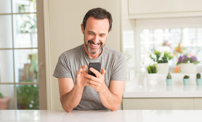 Middle age man using smartphone with a happy face standing and smiling with a confident smile...
