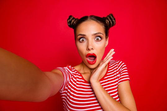OOPS! Self portrait of cute, trendy and shocked woman with bun hairdo wide open eyes mouth shooting selfie on front camera isolated on red background
